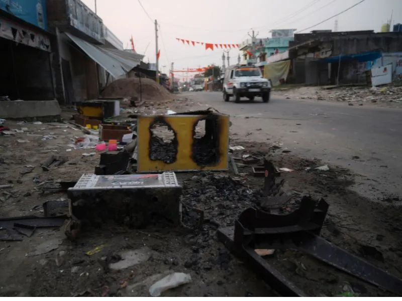 Image shows debris of burnt objects on the side of a road, with a police car passing on the road